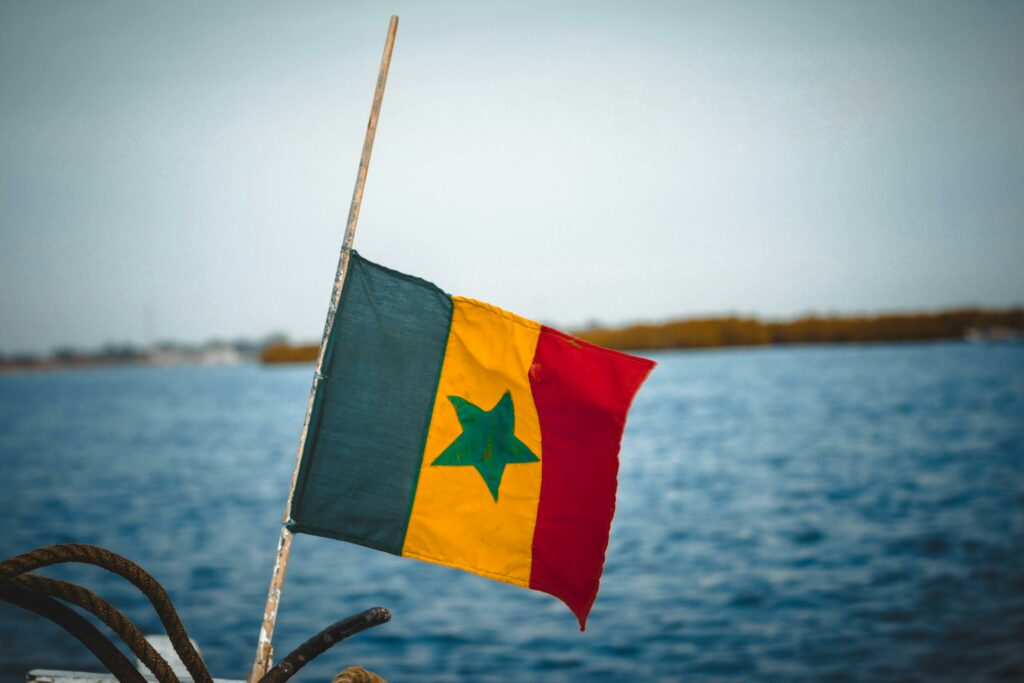 A vibrant Senegalese flag flutters against a serene sea backdrop, symbolizing national pride.