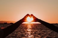 A romantic silhouette of hands forming a heart shape with the sun setting over İzmir's sea.